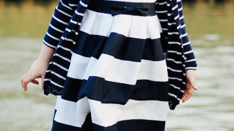 Ein gestreiftes Kinderkleid ist zu lang und wird von einem Mädchen, das am Wasser steht, getragen.