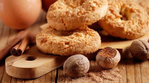 Kekse liegen auf einem Holzbrett, umgeben von Eiern, Zimtstangen und Muskatnüssen, die zum Backen inspiriert.