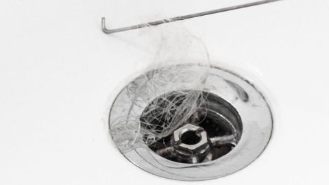 Ein Drahtkleiderbügel zieht Haare aus dem Abfluss, der mit Wasser und einer glänzenden Überlaufschicht umgeben ist.