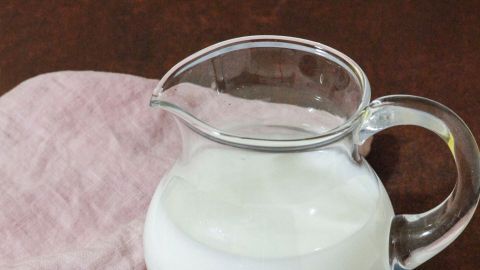Eine Glaskanne mit Vollmilch steht auf einem Tisch, daneben liegen Schokoladentafeln, umgeben von einem pinken Tuch.