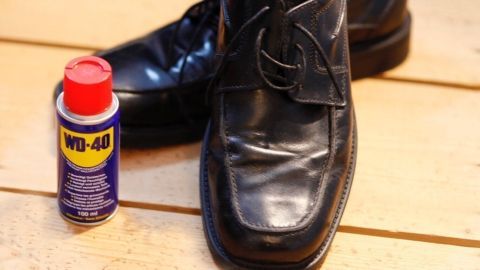 Schwarze Lederschuhe stehen auf einem hellen Holzboden, neben einer WD-40-Dose zur Imprägnierung.