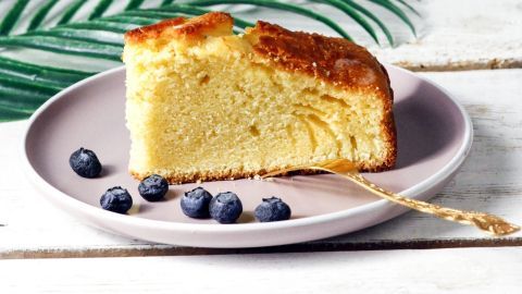 Ein saftiges Stück Kuchen mit Apfelmus auf einem lila Teller, umgeben von Blaubeeren und grünen Blättern.
