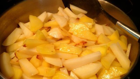In einem Kochtopf braten in Stücke geschnittene Kartoffeln, während eine Pfanne im Hintergrund steht.