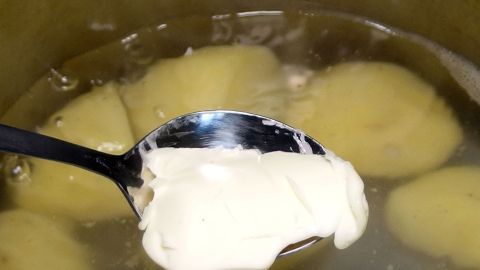 Im Kochtopf werden Salzkartoffeln gekocht, während ein Löffel mit Margarine darüber gehalten wird, um die Garzeit zu verkürzen.