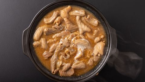 Ein schwarzer Topf enthält dampfendes, zartes Fleisch in einer würzigen Brühe, bereit zum Verzehr in einem gemütlichen Umfeld.