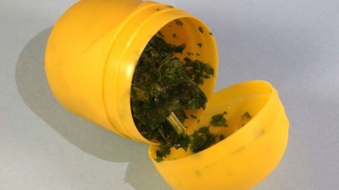 Ein gelbes Überraschungsei-Behälter liegt offen auf einer Oberfläche und enthält gefrorene Kräuter.