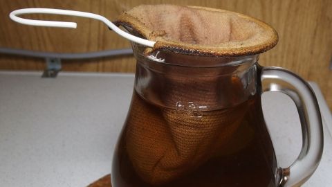 Ein Glas mit warmem Heiltee, der durch einen Stofffilter gezogen wird, steht auf einem Untersetzer in einer gemütlichen Küche.