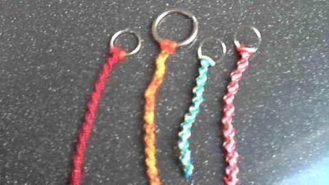 Vier bunte Schlüsselanhänger aus geflochtenem Material liegen auf einer dunklen Oberfläche, bereit für eine persönliche Note.