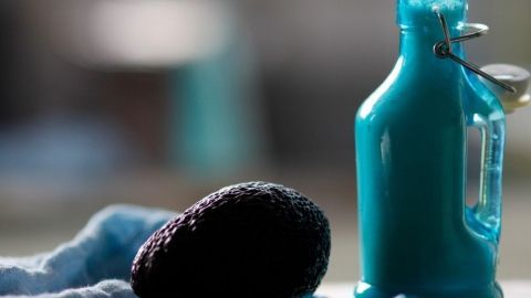 Eine reife Avocado liegt neben einer blauen Flasche in einer gepflegten Küche, bereit für eine verwöhnende Gesichtsmaske.
