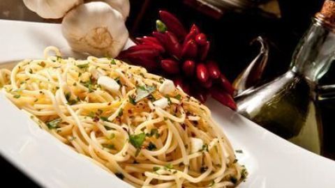 Ein Teller Spaghetti aglio e olio wird appetitlich angerichtet, umgeben von Knoblauch, Chilis und Olivenöl.