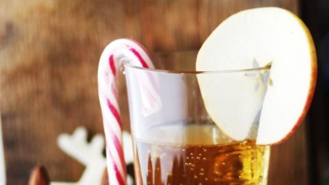 Ein Glas Apfel-Calvados-Punsch steht auf einem Teller, dekoriert mit Zimt und Weihnachtsfiguren in festlicher Umgebung.