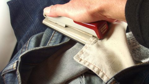 Wenn du in der Arbeit bemerkst, dass die Hosentasche ein Loch hat, kannst du bis zum richtigen Nähen die Stelle mit der Heftklammermaschine (Tacker) schließen. Ein Handwerker verwendet einen Hefter, um Stoffteile an einer Jeans zu fixieren, während er in einem hellen Raum sitzt.