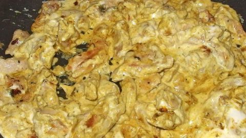In einer Pfanne brät Curry-Geschnetzeltes mit zarten Fleischstücken und einer cremigen Sauce, umgeben von Gewürzen.