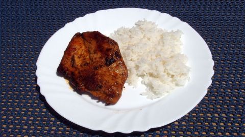 Saftiges Putensteak liegt auf einem weißen Teller neben einer Portion Reis, umgeben von einer strukturierten Oberfläche.