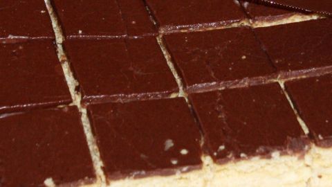 Mit dieser Methode bekommt der Schokoguss auf dem Kuchen einen ganz besonders schönen Glanz. Ein glänzender Schokoguss überzogen ein Schneidbrett mit gleichmäßigen Keksstücken, bereit zum Servieren.