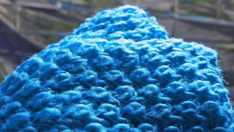 Ein blauer, gestrickter Pullover liegt relaxed, die Struktur zeigt sich deutlich, während er sanft im Licht schimmert.
