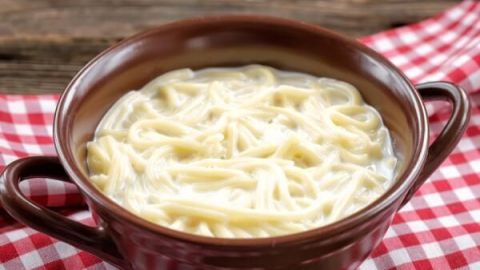 Braune Schüssel mit cremigen Milchnudeln auf rot-weiß kariertem Tuch, rustikaler Holzuntergrund.