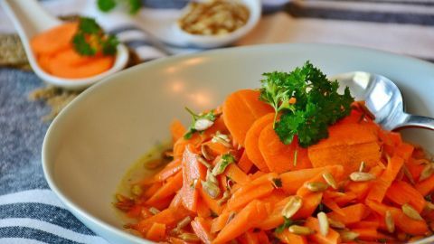 Ein bunter Möhrensalat aus frisch geraspelten Karotten und Kürbiskernen, garniert mit Petersilie in einer Schüssel.