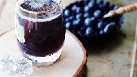 Ein Glas Heidelbeerpunsch steht auf einem Holzuntersetzer, umgeben von frischen Heidelbeeren in einer Schale.