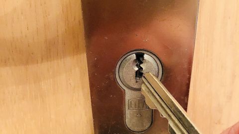 Ein Schlüssel wird in ein Schlüsselloch gesteckt, während er vor einer geschlossenen Holztür positioniert ist.