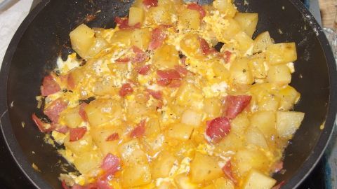 Eine Pfanne zeigt eine Mischung aus Eiern und Salami, die mit Kartoffeln angebraten wird, in einer modernen Küche.