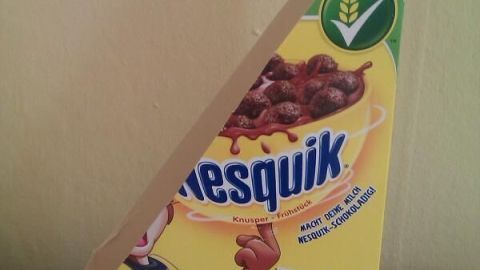 Eine kreativ gestaltete Cornflakes-Packung steht schräg auf einem Tisch und könnte als Zeitschriften-Sammler genutzt werden.