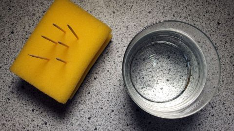 Ein gelber Schwamm liegt neben einem leeren Glas auf einer marmorierten Oberfläche, wobei der Schwamm für ausreichendes Trinken steht.