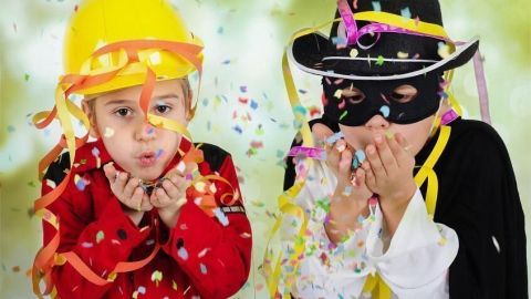 Kinder in Kostümen blasen Konfetti in die Luft. Links ein Junge im Bauarbeiterlook, rechts ein Kind als Zorro.