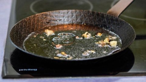 Eine eingebrannte Pfanne wird wieder sauber, wenn man Wasser in sie füllt und sie wieder auf die warme Herdplatte stellt. Dadurch löst sich die angebrannte Kruste. Eine verschmutzte Pfanne mit angebrannten Resten liegt auf einem Herd, bereit für eine schnelle Reinigung mit einem Trick.