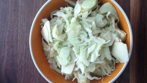 Ein Schüssel voller verblasster Fenchelblätter liegt mittig auf einem Holzuntergrund. Der Fenchelsalat ist frisch zubereitet.