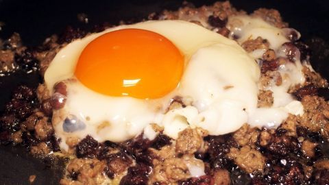 Ein Spiegelei liegt auf einer herzhaften Mischung aus gebratenem Kartoffeln und Zwiebeln, typisch für ein Bauernfrühstück.