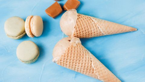 Zwei Karamelleis in Waffeln liegen auf einer blauen Oberfläche, umgeben von Macarons und Karamellstücken.