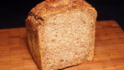 Vollkornbrot steht auf einem Holzbrett und zeigt eine rustikale, knusprige Kruste in einer gemütlichen Küchenszene.