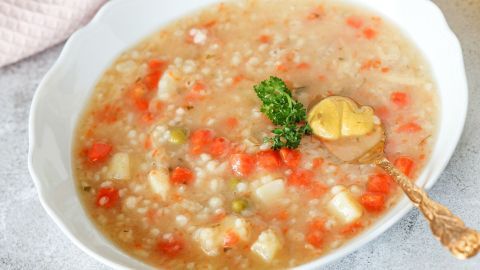Pikante Graupensuppe mit Senf wird in einer Schüssel serviert, garniert mit Petersilie und einem Löffel Senf.