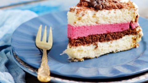 Ein Stück bunt geschichteter Kuchen liegt auf einem blauen Teller, daneben steht eine vergoldete Gabel.