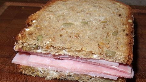 Ein Sandwich aus Vollkornbrot mit Schinken liegt auf einem Holzbrett, während der Fokus auf der Reduzierung von Schulbrotverschwendung liegt.