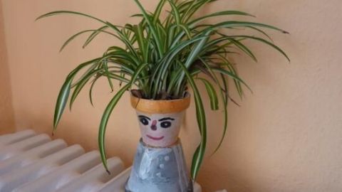 Ein origineller Blumentopf aus einem bemalten Behälter steht auf einem Heizkörper, beherbergt eine Pflanze und wirkt freundlich.