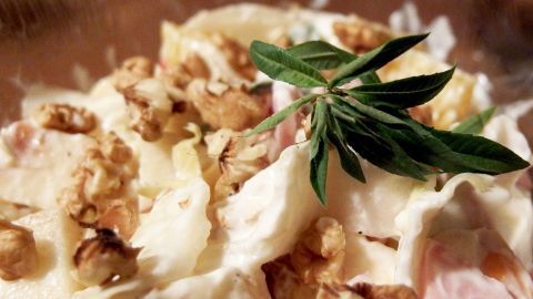 Ein frischer Chicoree-Salat mit Orangen, Bananen und Walnüssen wird appetitlich serviert, garniert mit einem Kräuterblatt.