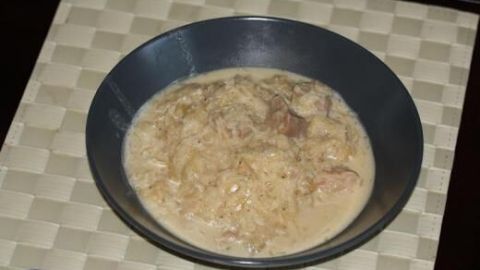 Ein Szegediner Gulasch serviert in einer dunklen Schale, auf einem geflochtenen Tischset, mit einem Löffel an der Seite.