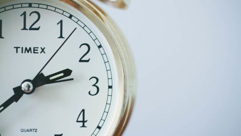 Eine goldene Uhr zeigt die Zeit an, während sie gegen einen hellen Hintergrund positioniert ist, der an Wecker erinnert.