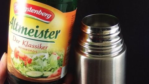 Ein grüner Essigflasche wird über eine offene Thermoskanne gehalten, um Gestank zu entfernen. Der Hintergrund ist dunkel.