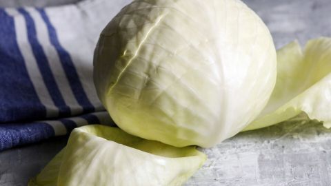 Ein Kopf Weißkohl liegt auf einer flachen Oberfläche, während einige Blätter locker daneben liegen, um das Entblättern zu zeigen.