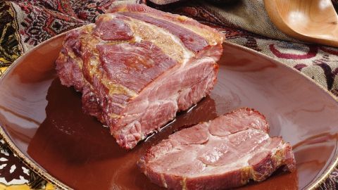Der Kasslerbraten liegt auf einem rustikalen, braunen Teller, während ein Stück geschnitten daneben präsentiert wird.