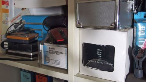 Ein Regal voller gebrauchter Elektronikgeräte und Kartons, die auf ein Ausmisten beim Umzug hindeuten.