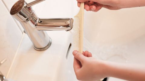Ein Kamm wird unter einem Wasserstrahl gehalten, während er sich über dem Waschbecken befindet.