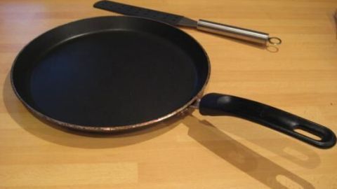 Eine flache Pfanne liegt auf einer Holzoberfläche, bereit zum Zubereiten von herzhaften oder süßen Crêpes.