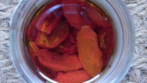 Getrocknete Tomaten schwimmen in Öl in einem Glas, das auf einem strukturierten Untergrund platziert ist.