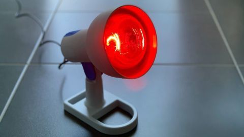 Eine rot leuchtende Infrarotlampe steht auf dem Boden und erzeugt Wärme zur Linderung von Beschwerden bei wundem Po.