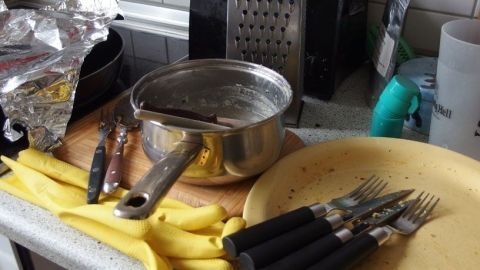 Auf der Arbeitsplatte stehen ein Kochtopf und ein Teller mit Besteck, während Bananen und Küchenutensilien umherliegen.