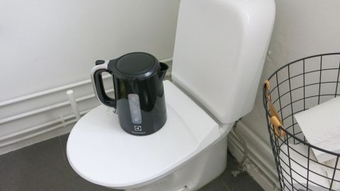 Ein Wasserkocher steht auf einem geschlossenen Toilettensitz, bereit, kochendes Wasser für einen verstopften Abfluss zu verwenden.